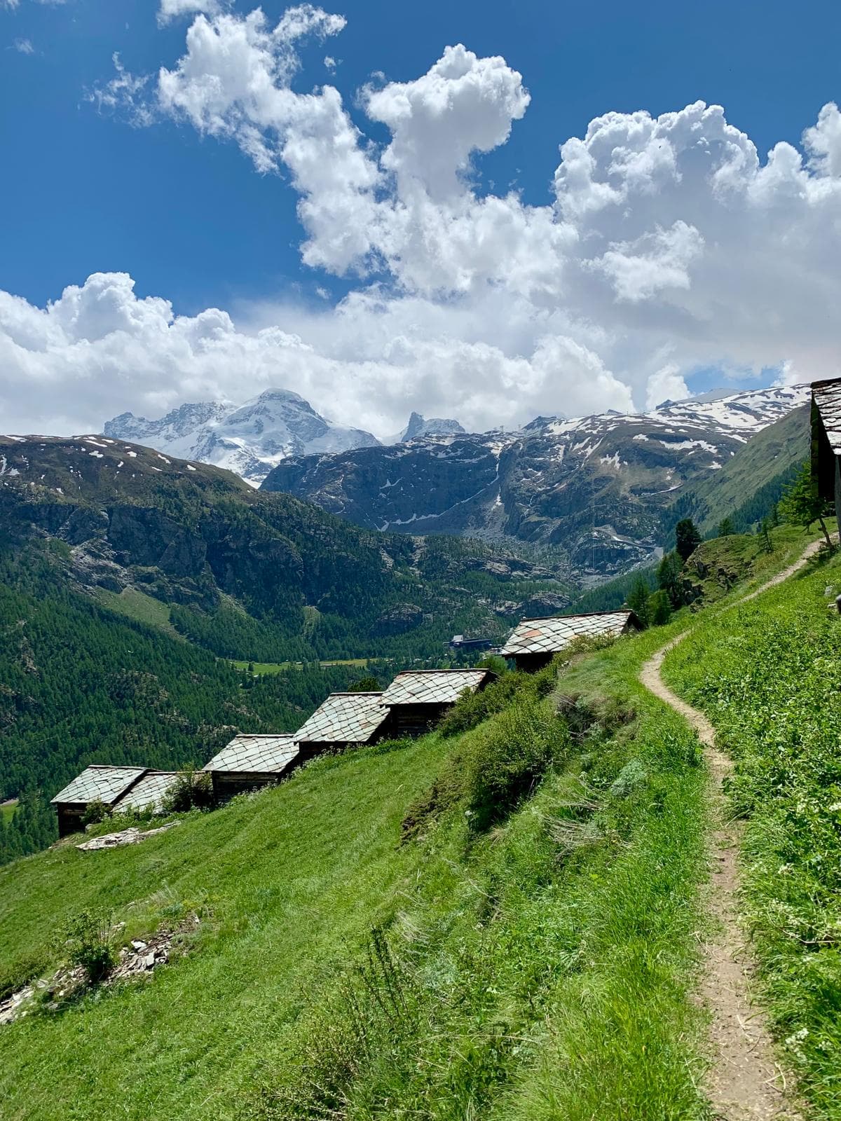 Alpine trail past stone huts beneath snowy peaks